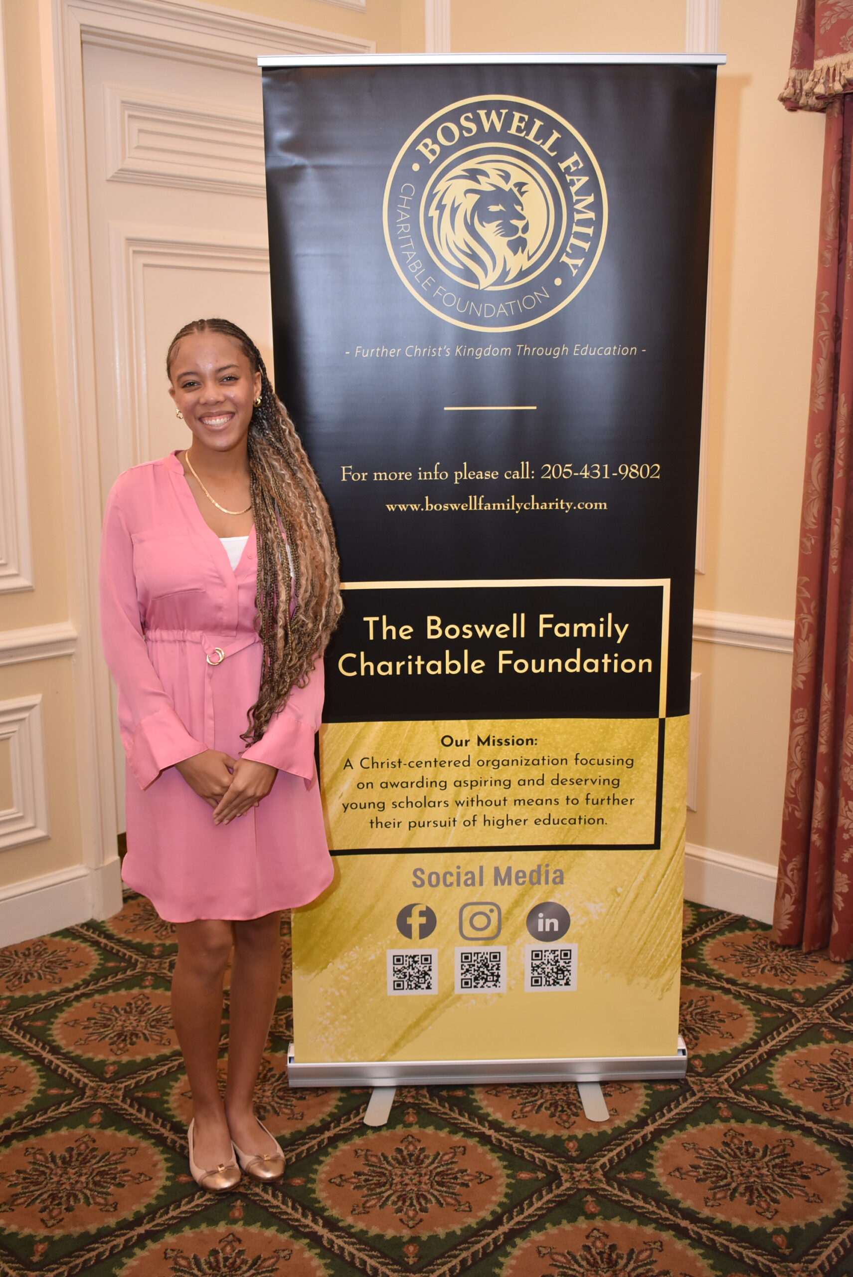 A smiling Triniti Fuller, a 2024 Boswell Family Charitable Foundation scholarship recipient, stands next to the foundation's banner.