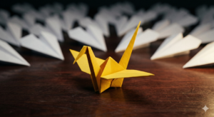 A single yellow origami crane standing out in front of a large group of white paper airplanes on a wooden surface.